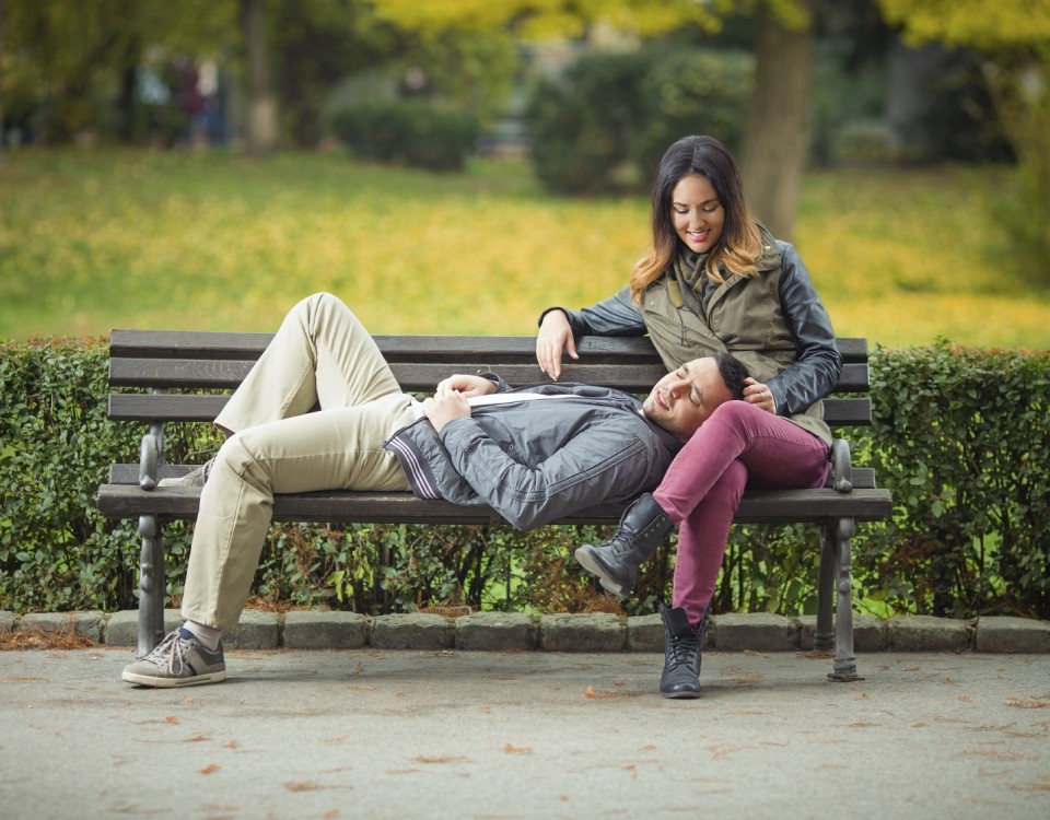 Spending your time, Happy young woman sitting on a bench in a park with her boyfriend lying on her lap